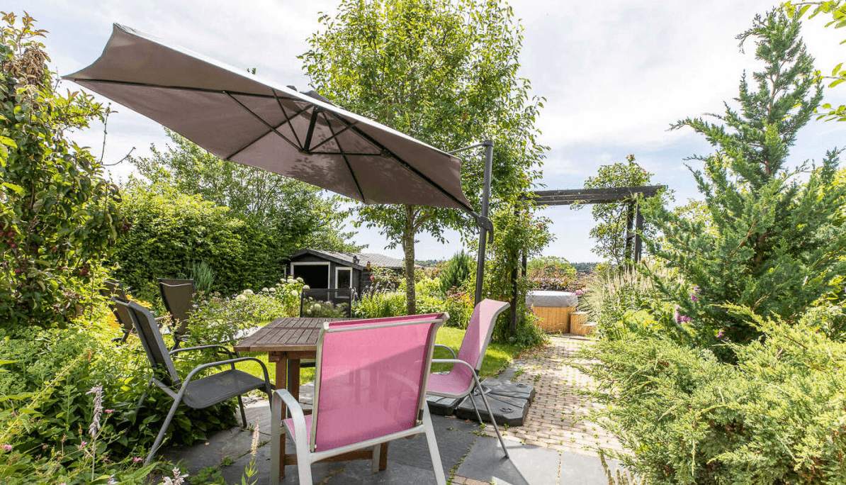 Terrasse du domaine : table et chaises de jardin sous parasol, allée pavée et bain nordique sous pergola au fond