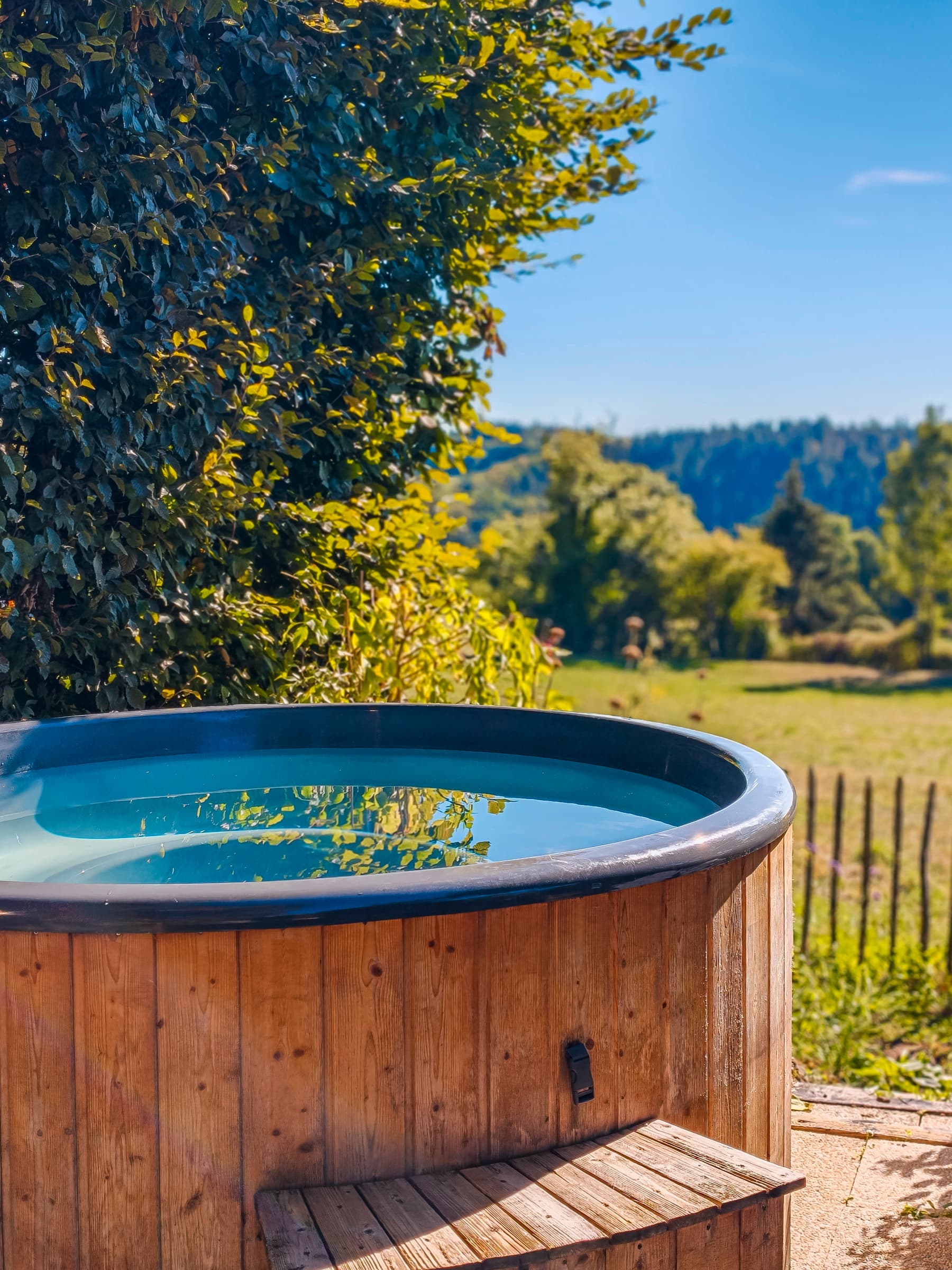 Bain nordique en bois du jardin partagé d’Annabelle et Rose, face aux prés et aux collines.
