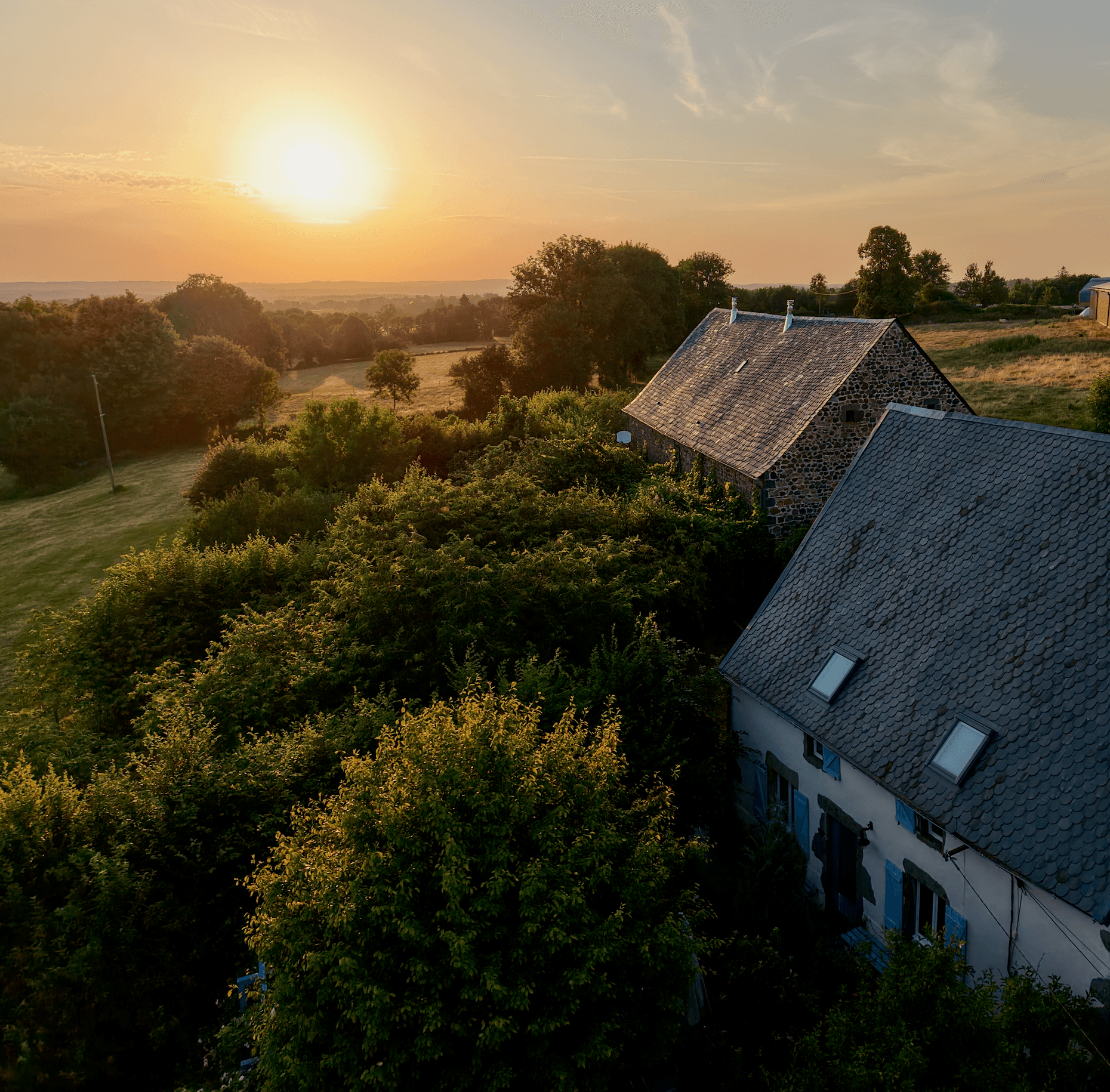 Vue aérienne du Domaine des Roses au coucher du soleil : gîtes en pierre, jardin et collines de l’Artense
