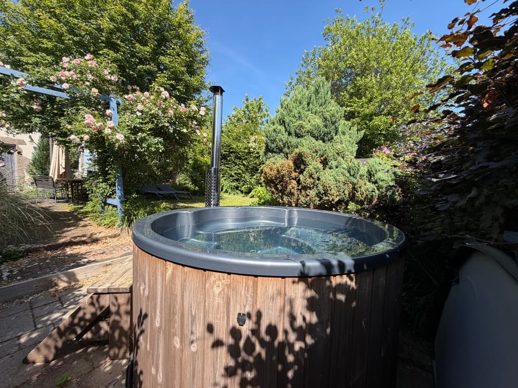 Bain nordique chauffé au bois, niché dans le jardin entre rosiers et arbres