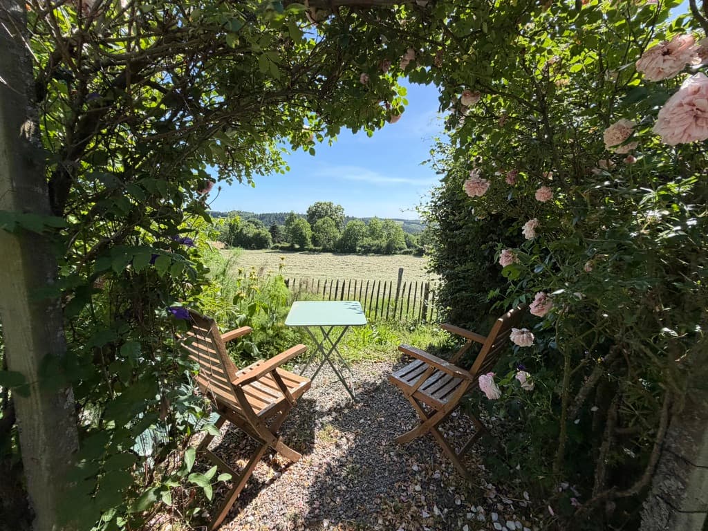Coin détente avec chaises en bois et vue sur la campagne, encadré par des rosiers